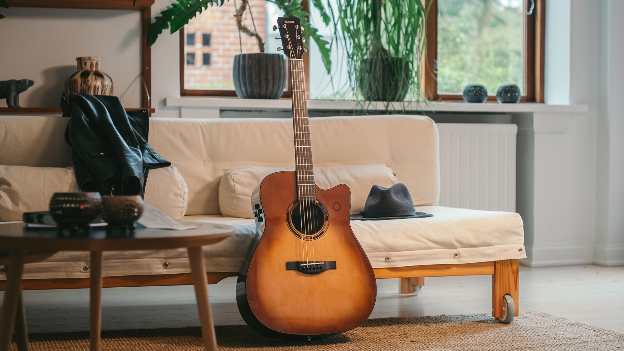 Guitar acoustic TAG3 C được đặt trên ghế sofa cùng một chiếc túi bên cạnh.