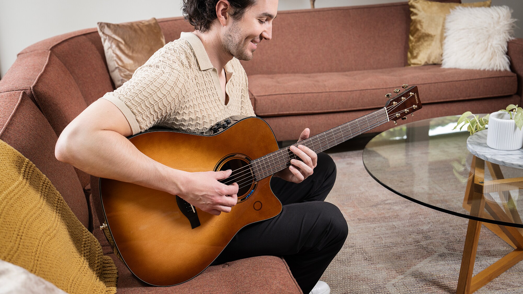 Một người đàn ông ngồi trên sofa trong phòng khách đang chơi guitar acoustic TAG3 C